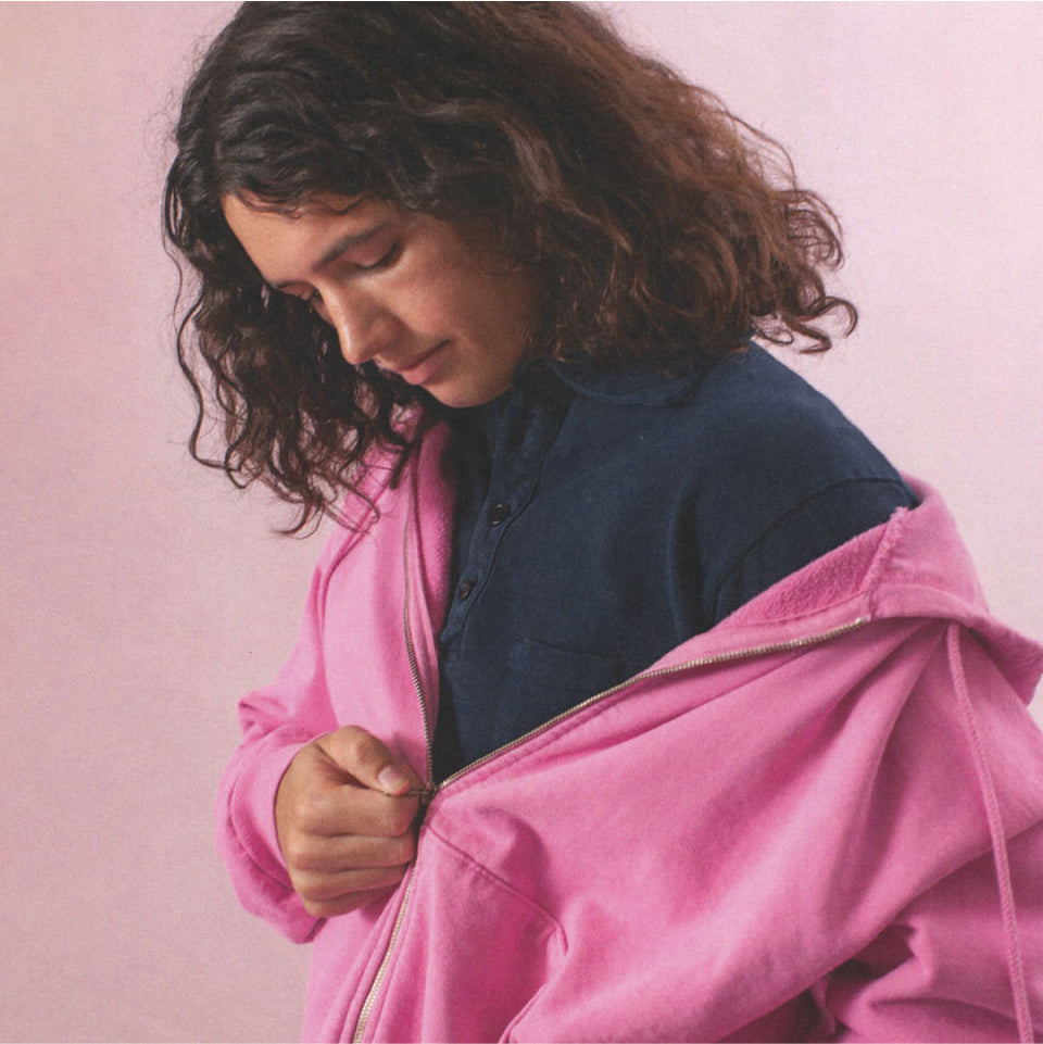 Person wearing a Pixie Trash Zip Up Hoodie over a Juniper Rugby Trash Polo against a pink background.