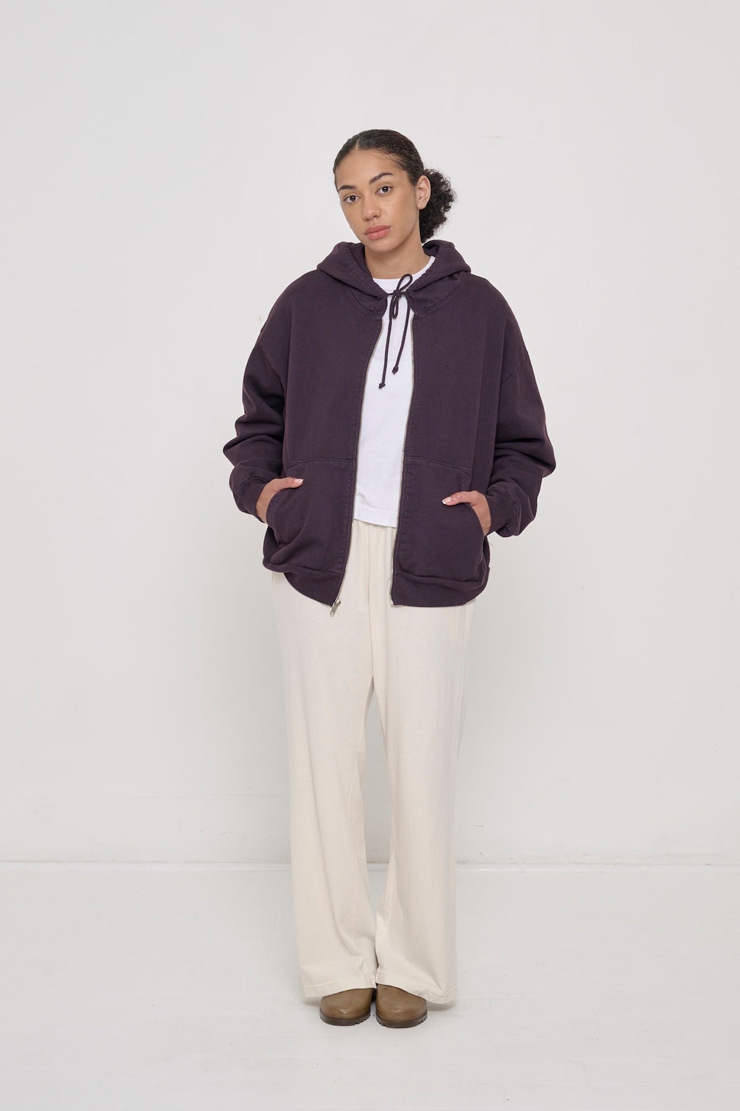 Person wearing an unzipped Mulberry Trash Zip Up Hoodie with both hands in kangaroo pockets and drawcord tied in a bow. 