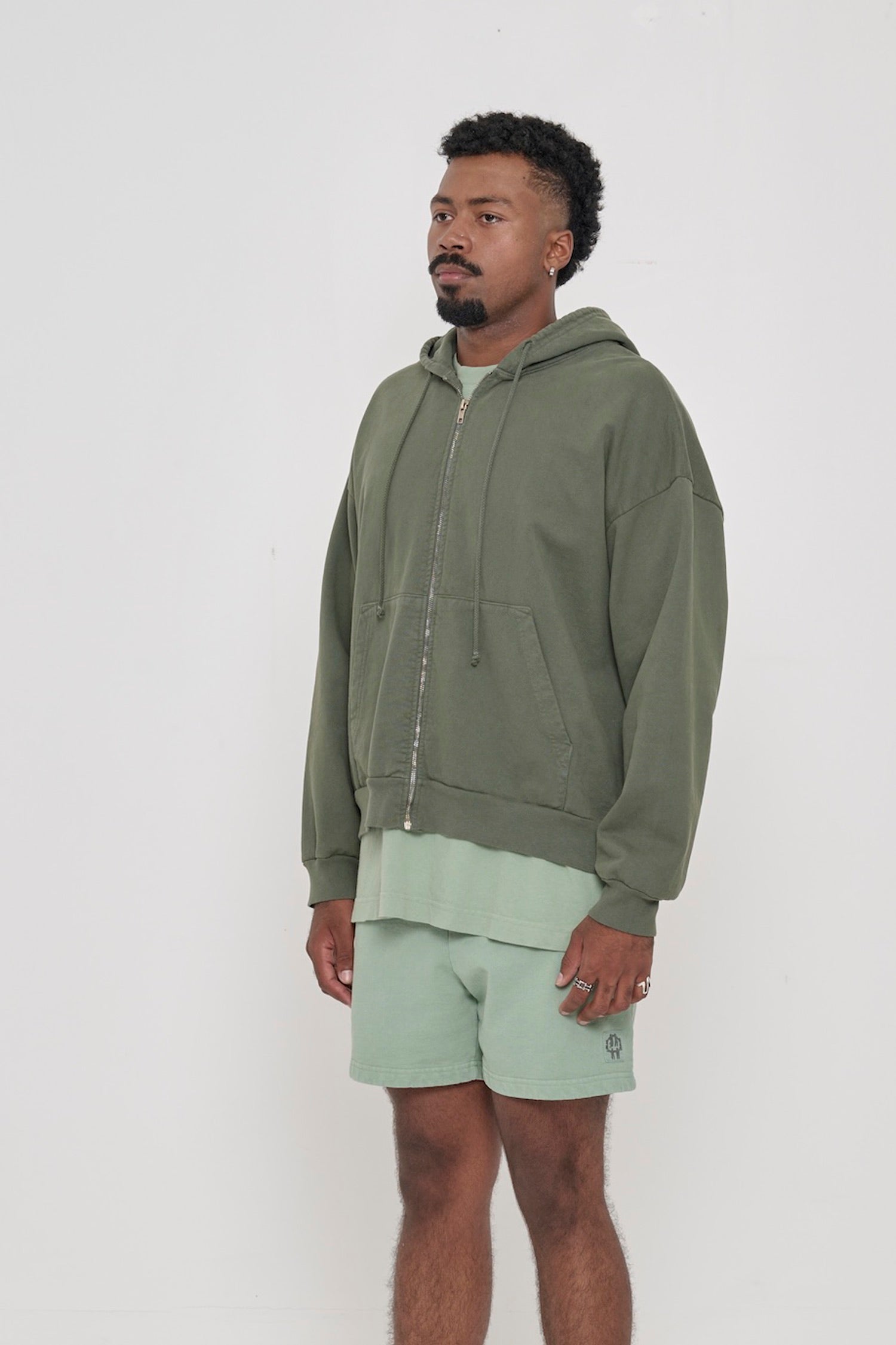 Person facing 45-degrees, wearing a Pine Trash Zip Up Hoodie, showcasing sleeve's relaxed fit and drop shoulder.