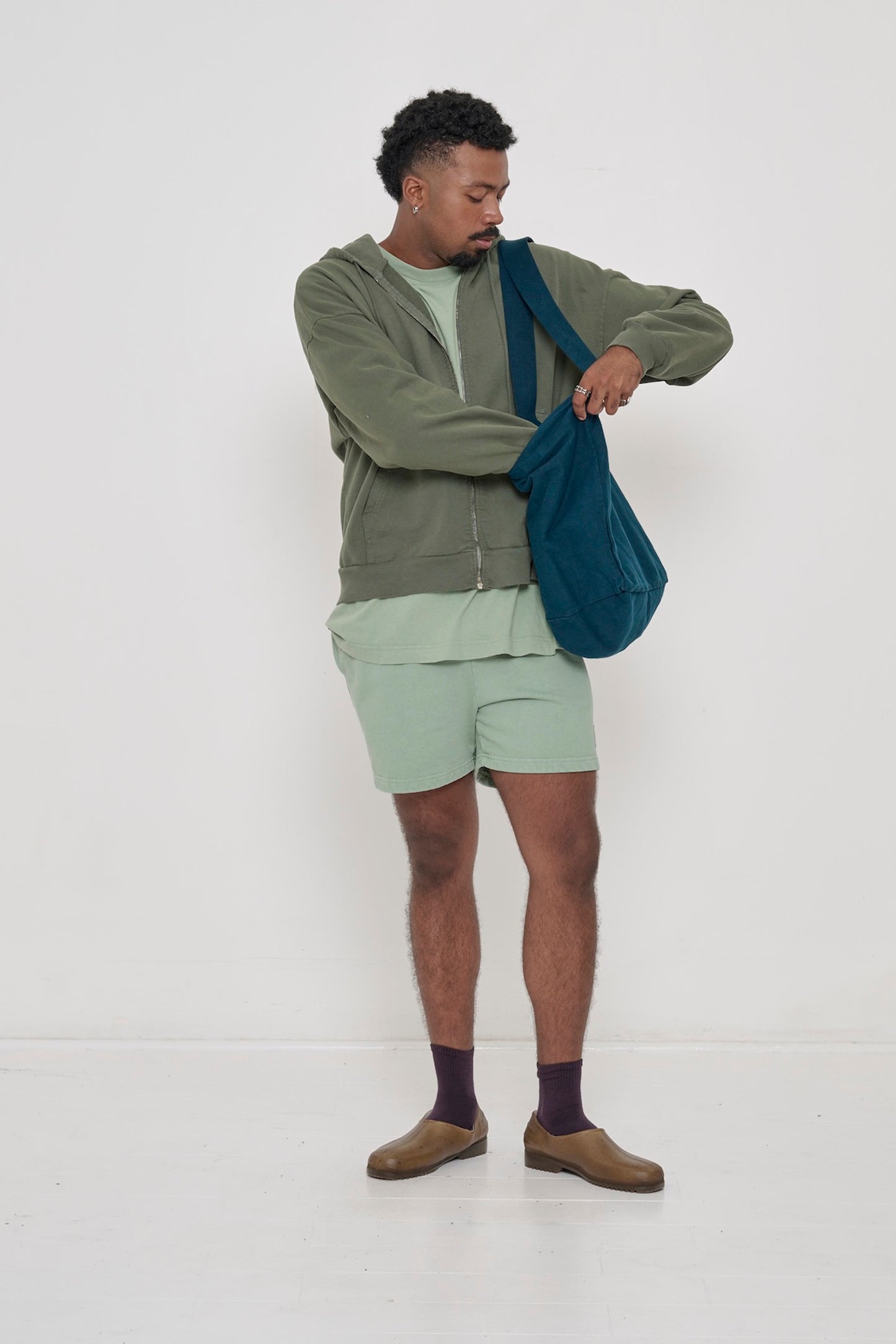Person wearing Pine Trash Zip Up Hoodie half zipped with Wasabi Trash Fleece Everyday Shorts. 