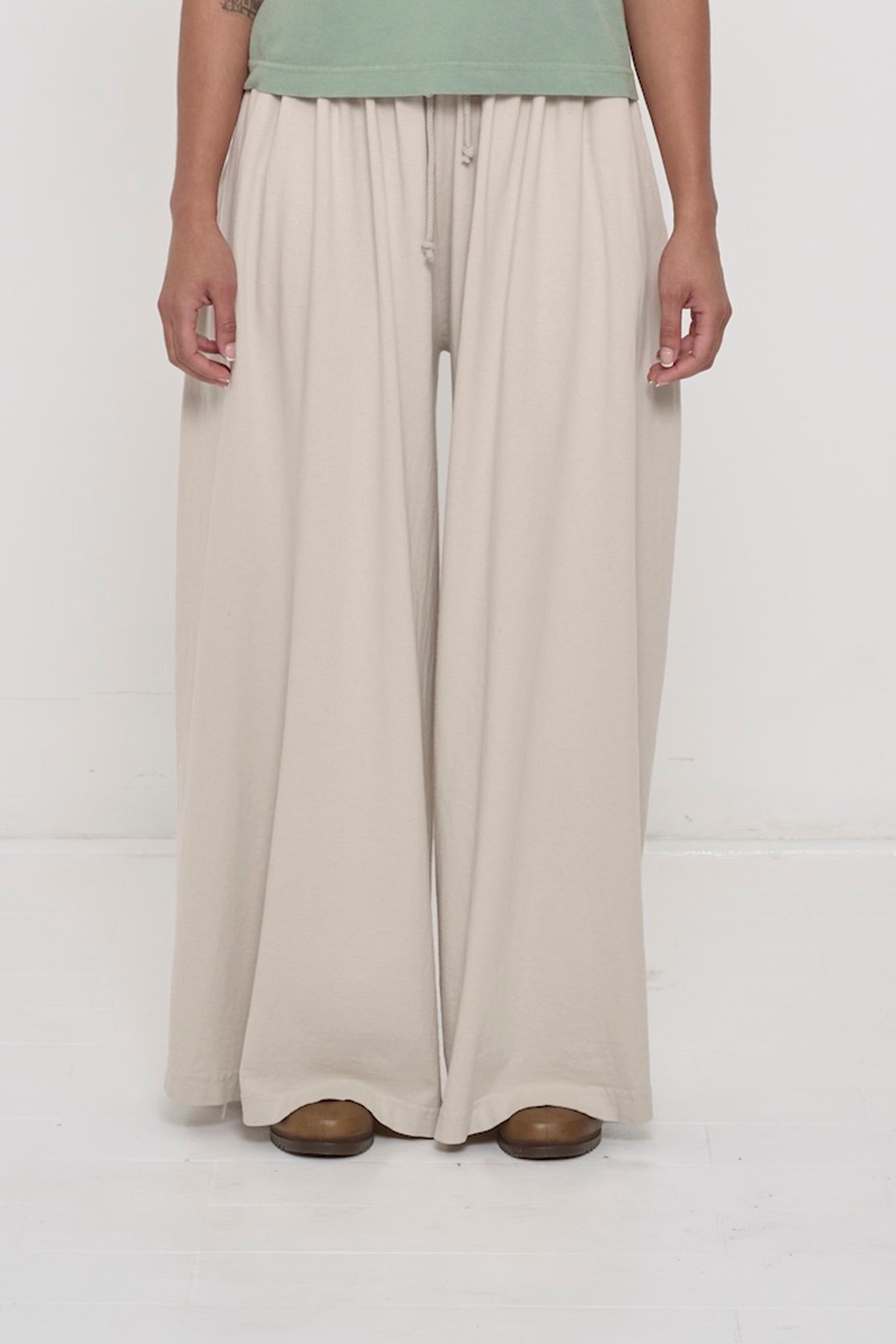 Front view of a person in Oat Tubular Pants, featuring elastic waistband, drawcord, relaxed drape.