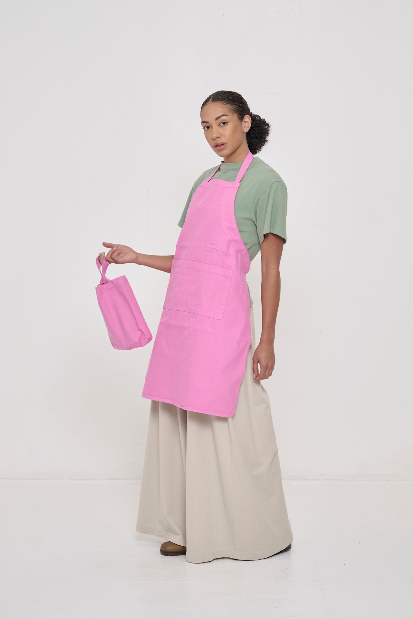 A person wearing Oat Tubular Pants and a Pixie Adjustable Apron and Pixie Loop Tote.