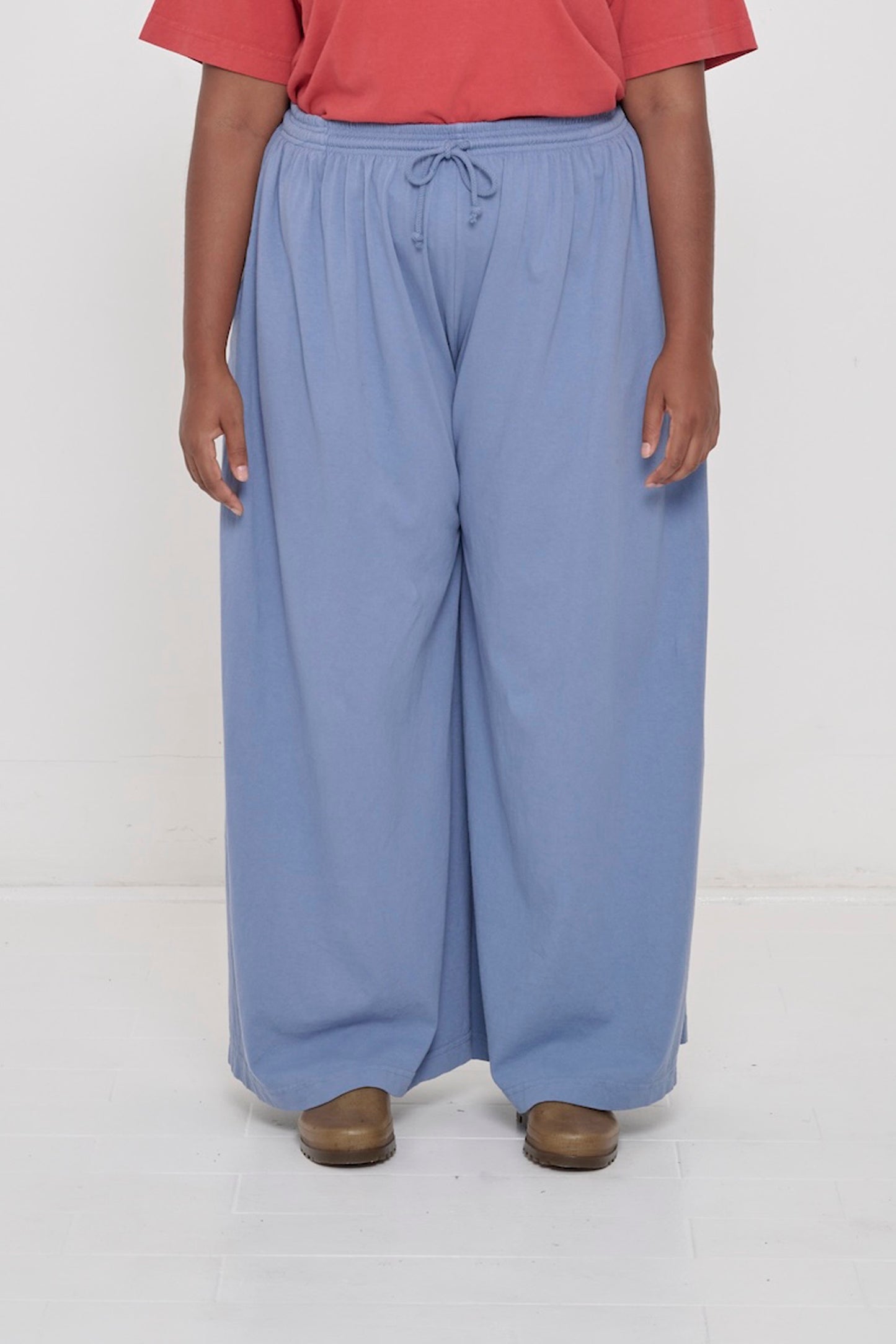 Front view of a person in Periwinkle Tubular Pants, featuring elastic waistband, drawcord, relaxed drape.