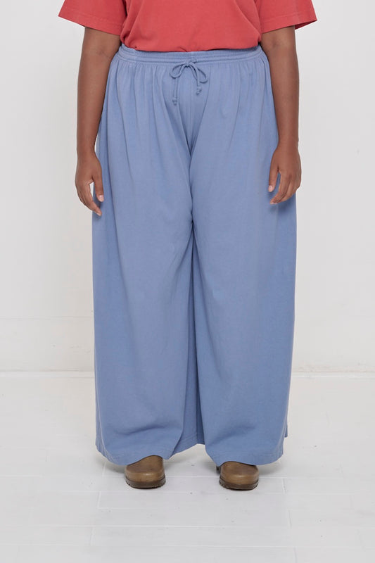Front view of a person in Periwinkle Tubular Pants, featuring elastic waistband, drawcord, relaxed drape.