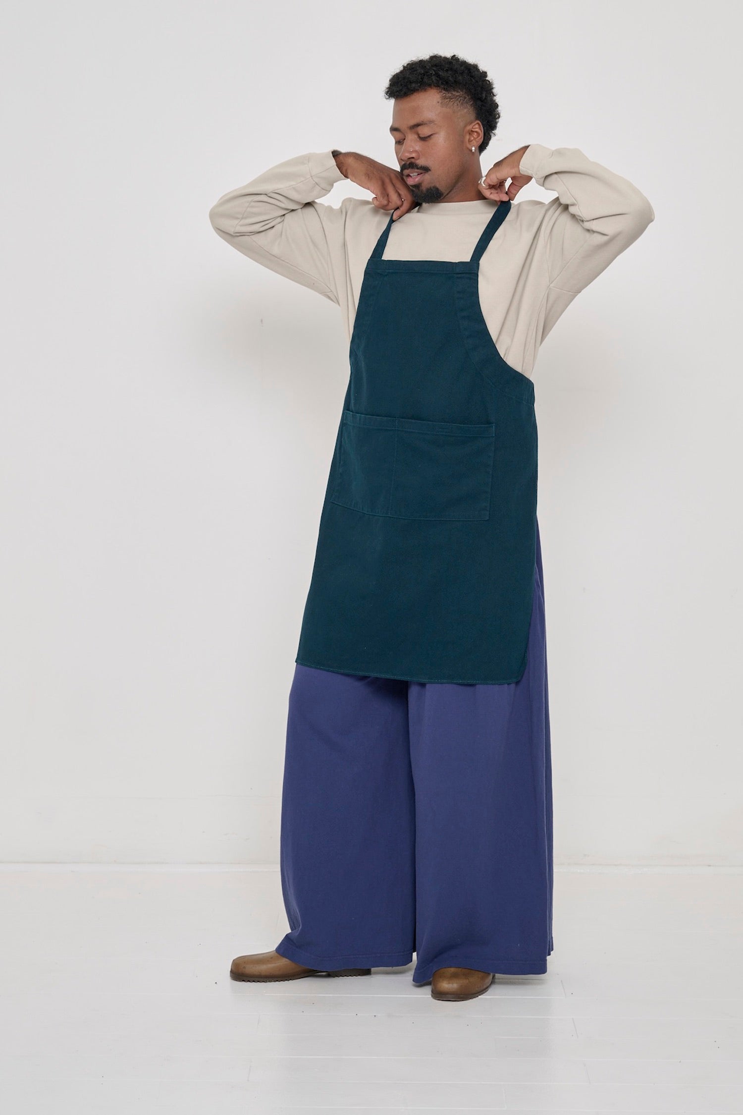 A person wearing Washed Navy Tubular Pants and a Juniper Adjustable Apron. 
