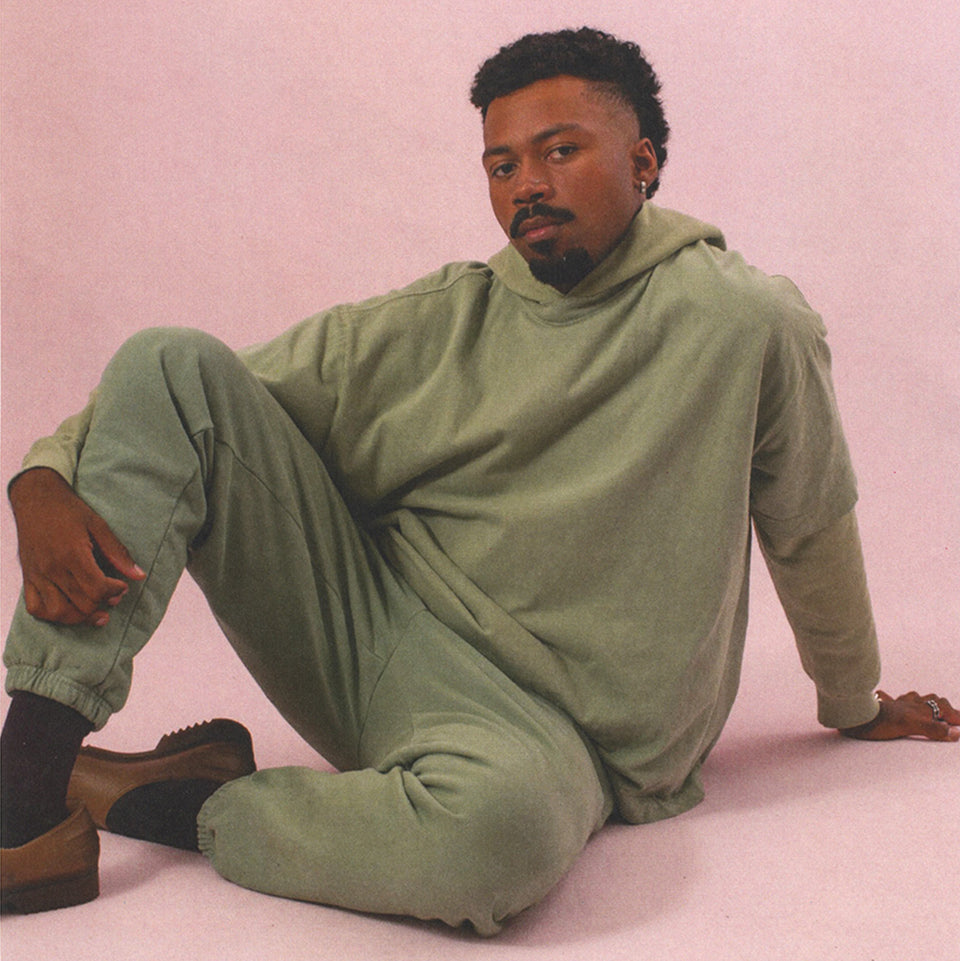 Man sitting on ground, wearing Boxier Trash Tee, Trash Hoodie and Trash Sweatpants in Wasabi.