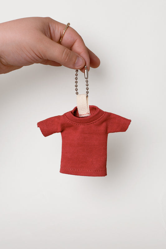 Red t-shirt keychain held by a hand against a light gray background
