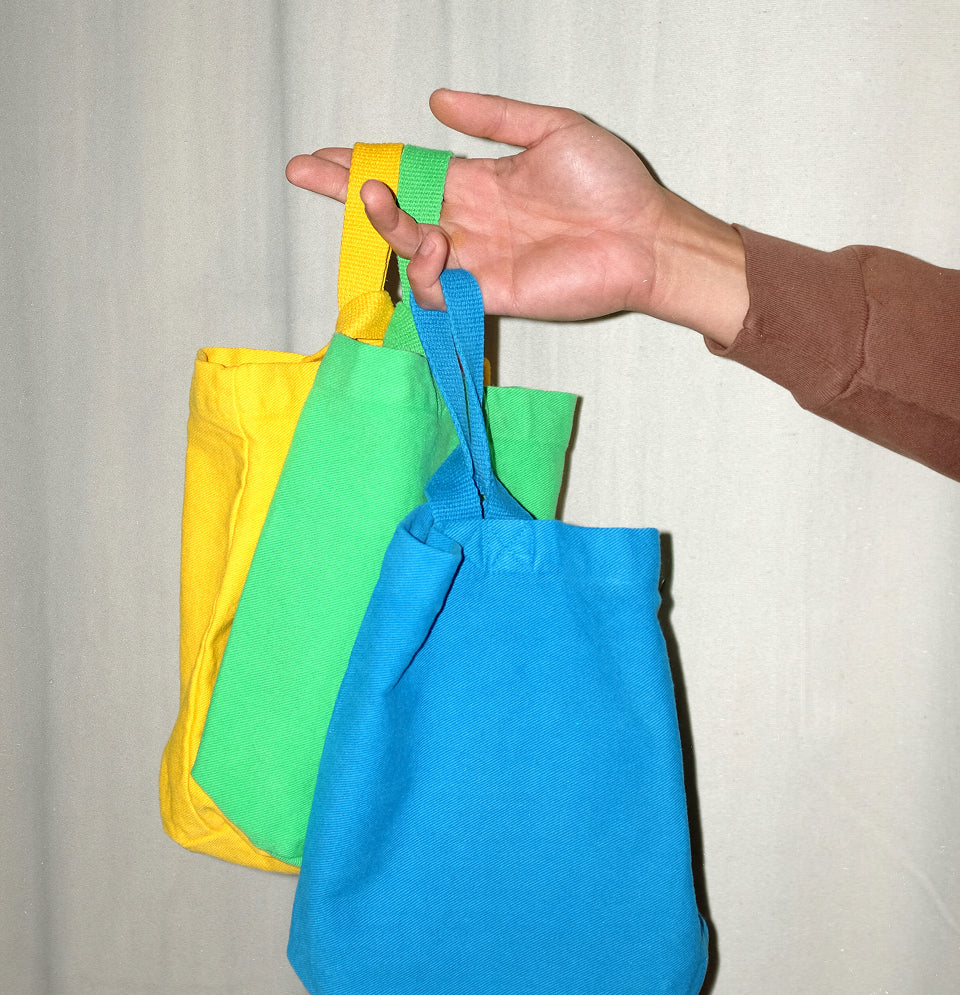 Hand holding Loop Totes in Everybody Yellow, Nice Grass, and Malibu.
